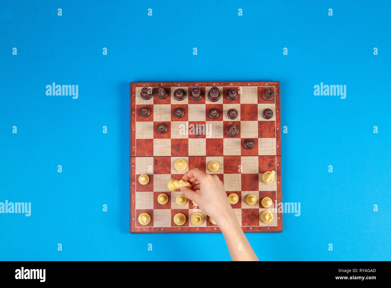 Kid mains sur un échiquier jouant aux échecs sur fond bleu, vue d'en haut Banque D'Images