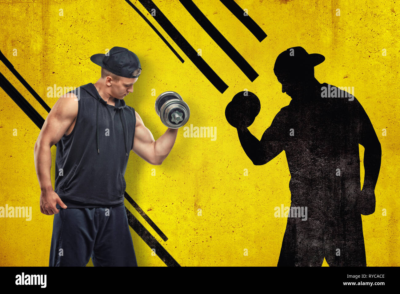 Strong muscular young man in black sportswear avec un haltère avec ombre noire sur fond jaune Banque D'Images