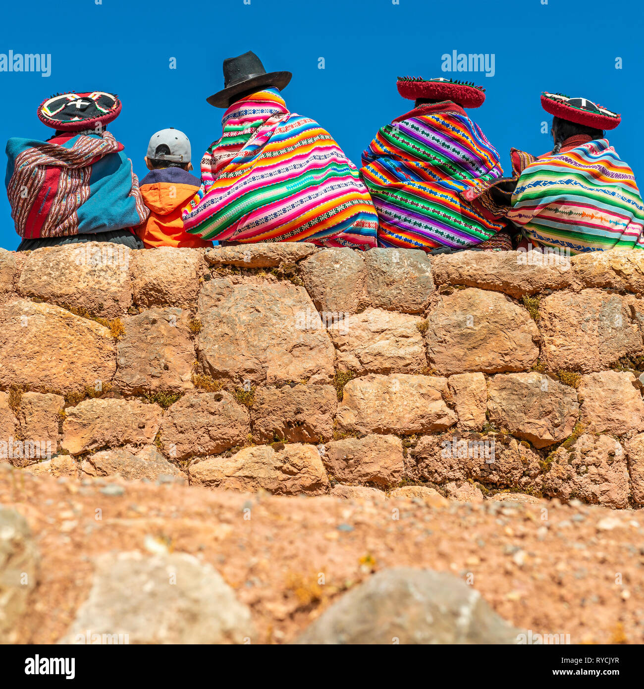 Photographie de la place des peuples quechua mesdames en costume traditionnel avec un jeune garçon assis sur un mur Inca dans la Vallée Sacrée des Incas, au Pérou. Banque D'Images