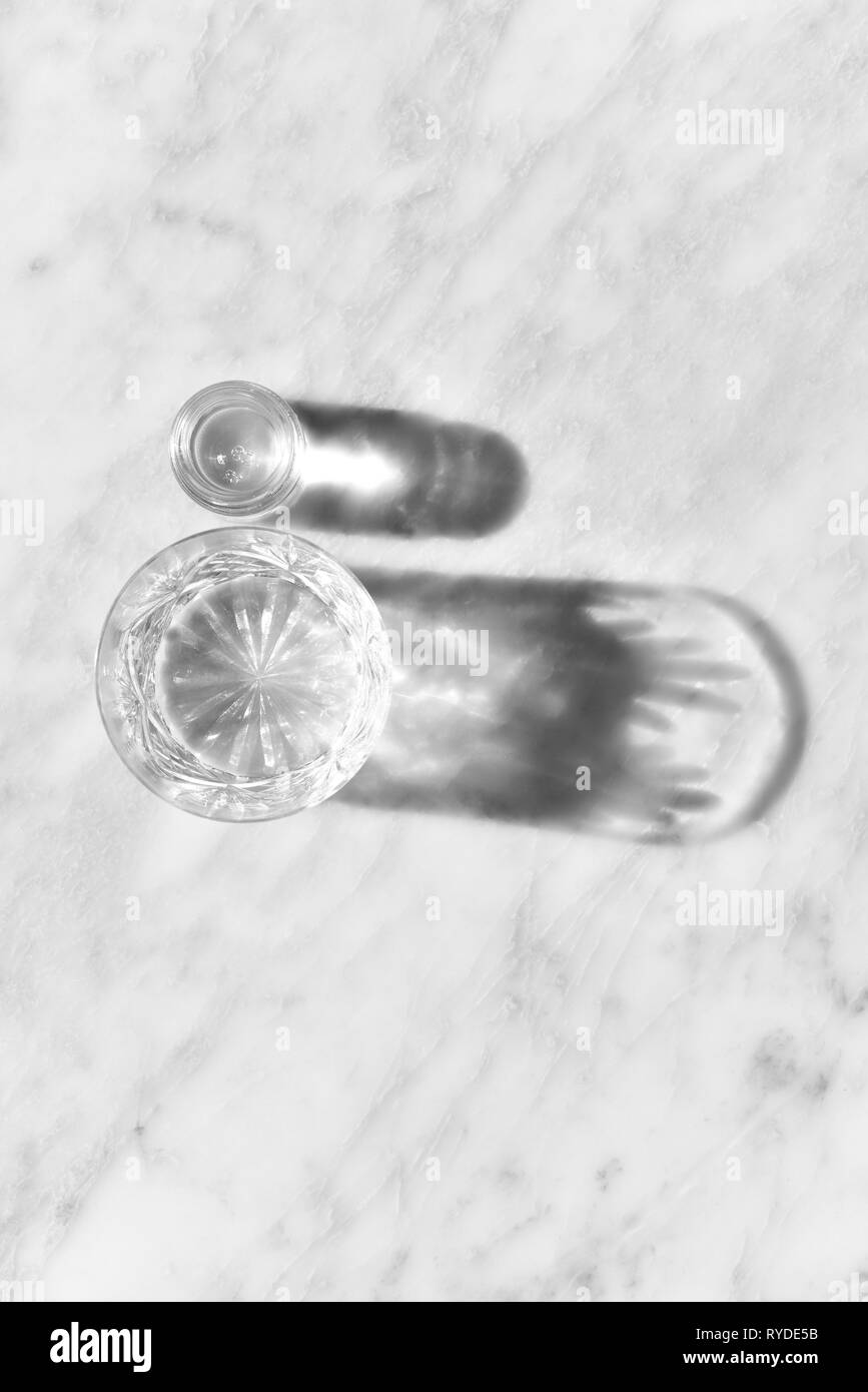 Un verre d'eau en plein soleil avec des ombres projetées sur un fond de marbre Banque D'Images