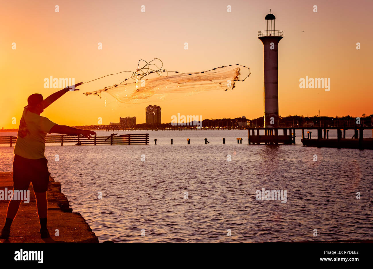 Un homme jette une nette brill au Broadwater Beach Marina au coucher du soleil sur le phare du port de plaisance, le 24 février 2019 à Biloxi, Mississippi. Banque D'Images