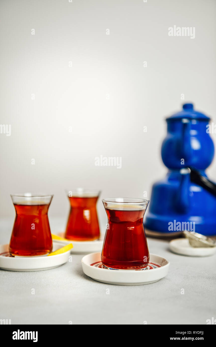 Du thé turc servi dans trois verres à thé turc, de fines tranches de citron sur le côté de deux. Accompagné d'une théière bleu nostalgique. Banque D'Images