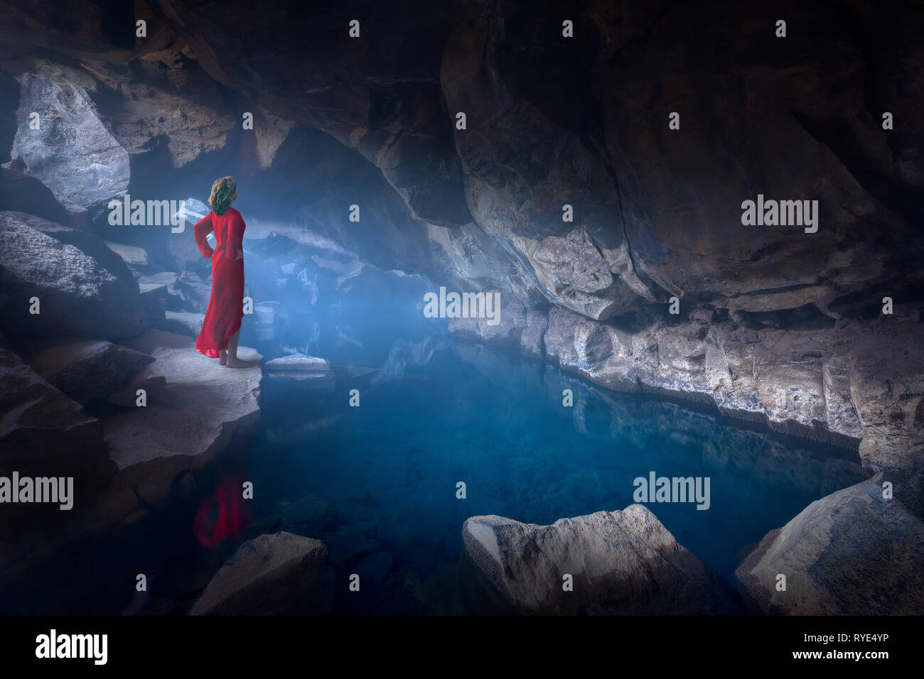 Paysage d'Islande fine art photo de dame en robe rouge trônant fièrement en spooky et misty grotte avec bain d'eau bleue. Banque D'Images
