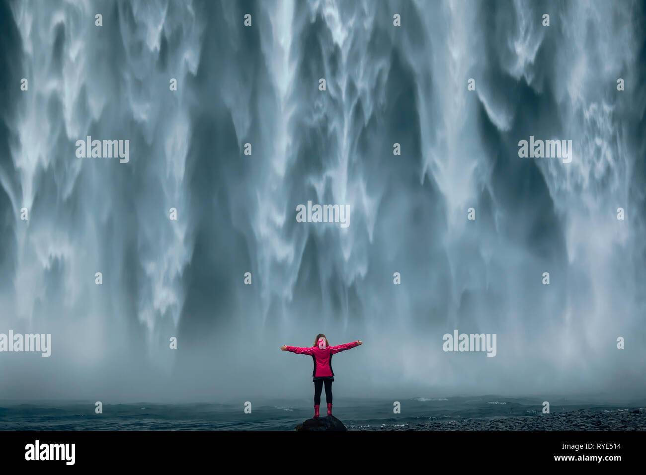 Paysage d'Islande photo de brave fille qui trônant fièrement avec son bras levés en face de mur d'eau de cascade puissante. Banque D'Images