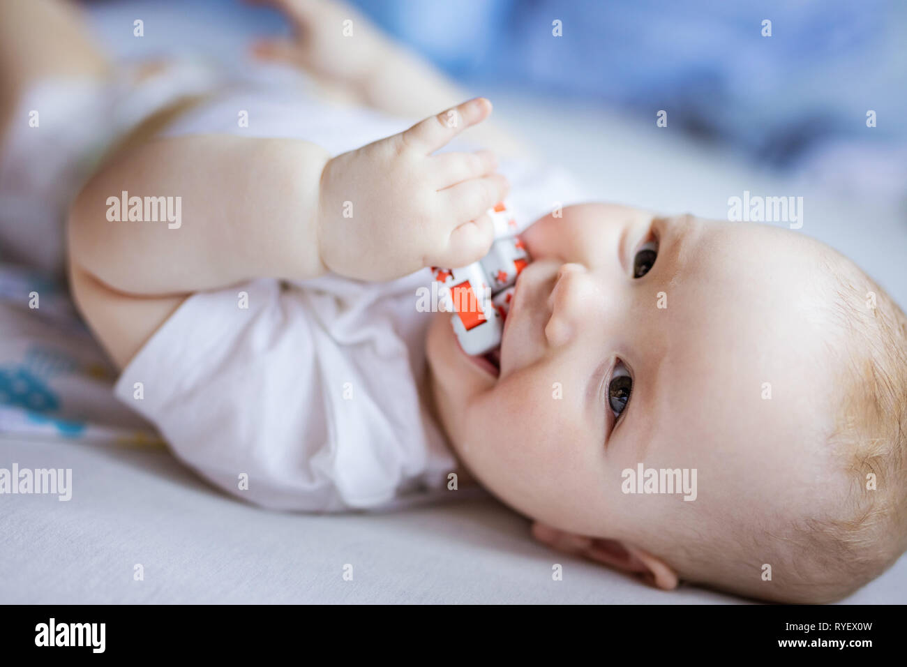 Cute baby girl Playing with toy, looking at camera et souriant tout en étant allongé sur le lit chez lui Banque D'Images