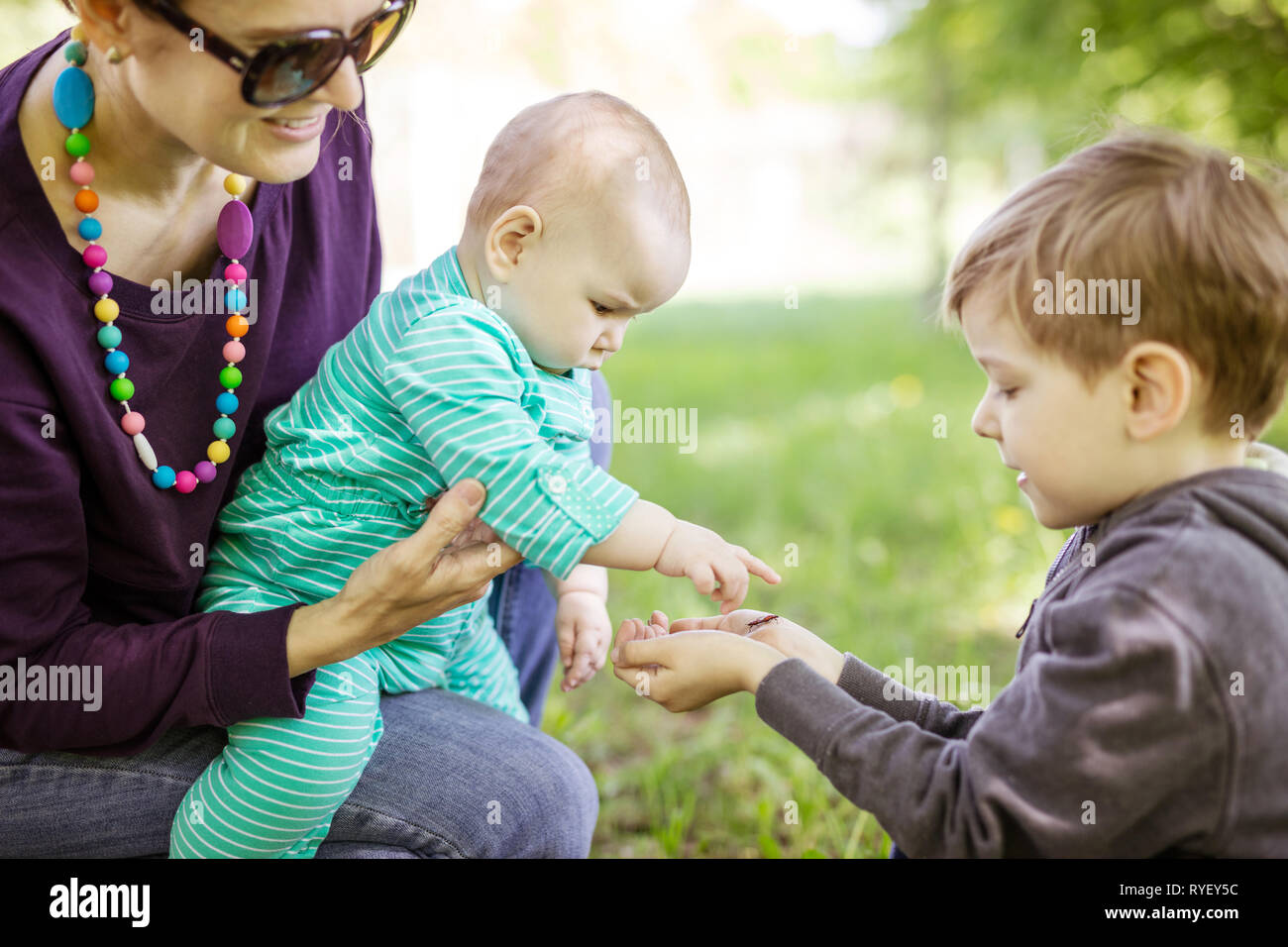 Portrait of young woman holding baby fille tout en montrant d'âge préscolaire bugs sur sa main. Temps libre dans le parc. Profiter de la famille belle journée d'outdo Banque D'Images