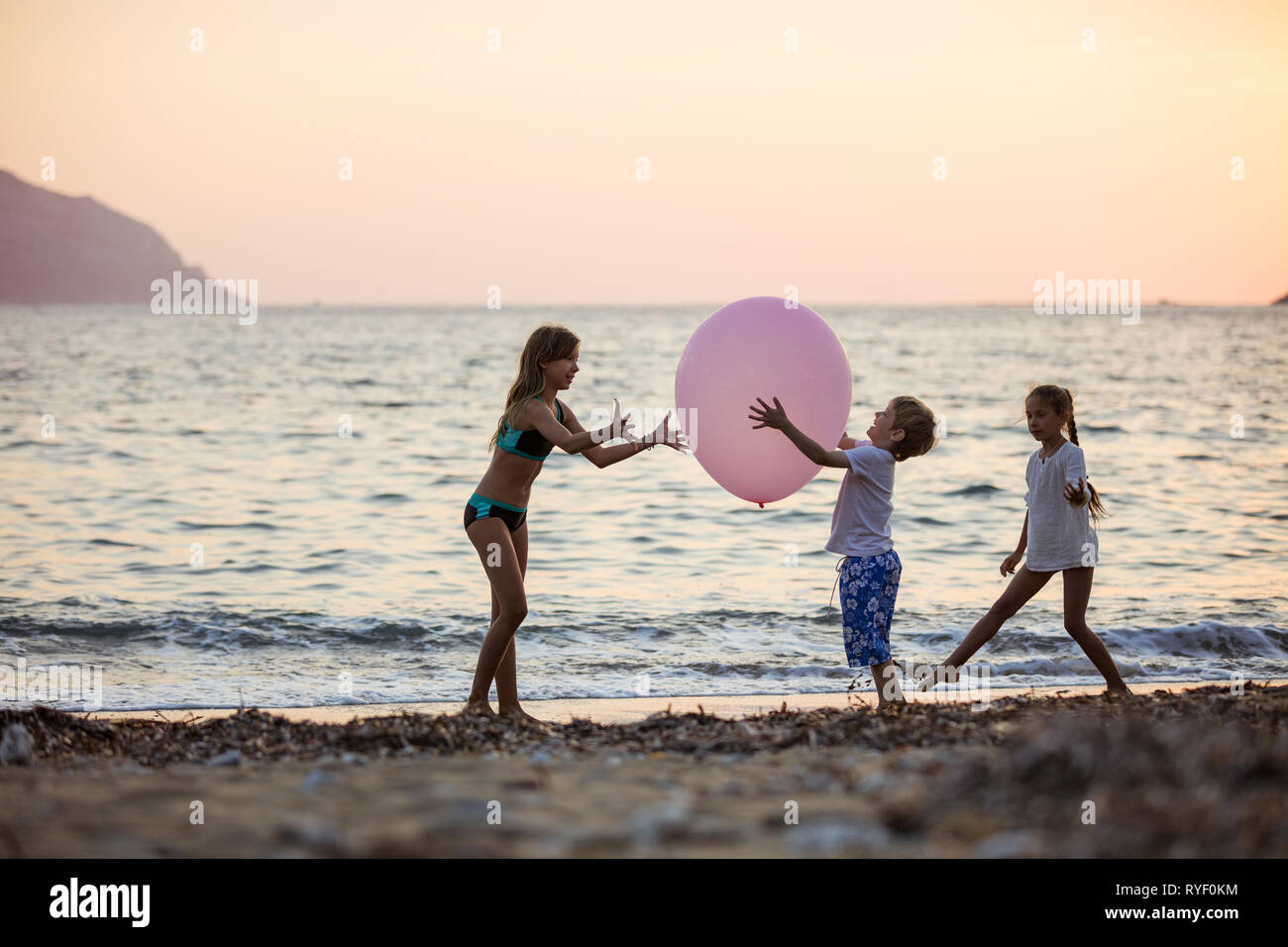 Trois enfants jouant avec un énorme ballon rose sur la plage au coucher du soleil Banque D'Images