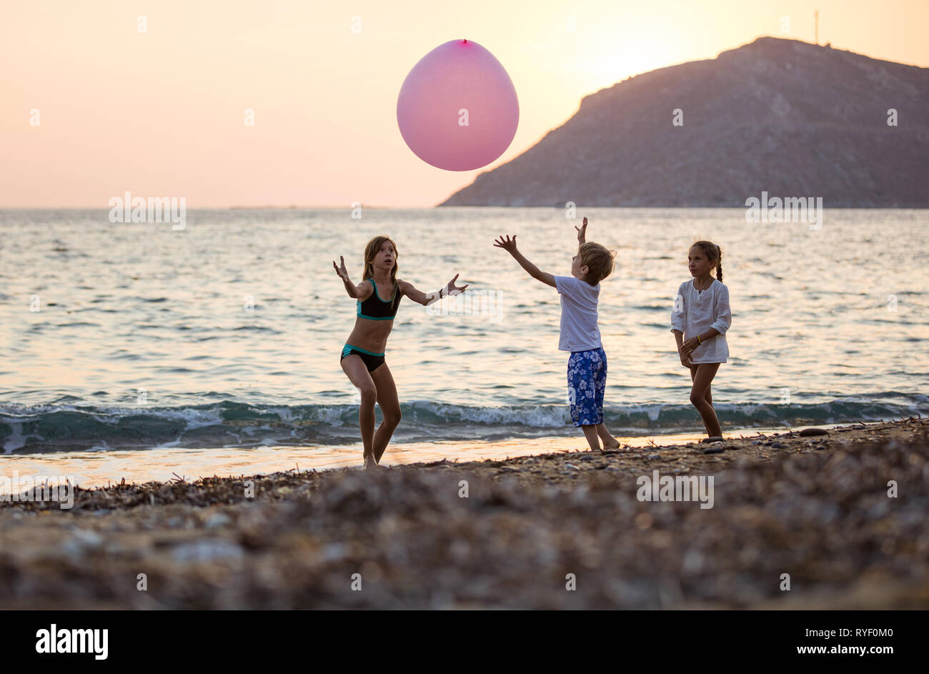 Trois jeunes enfants jouant avec un énorme ballon rose sur la plage au coucher du soleil Banque D'Images