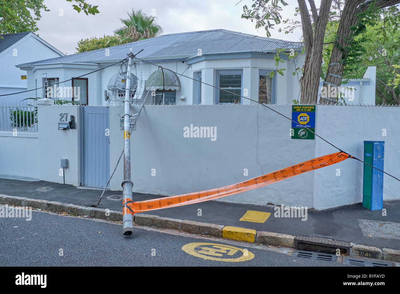 Poteau et fils tombés à une clôture et mur maison sur coin de rue dans la banlieue sud de Cape Town, Afrique du Sud Banque D'Images