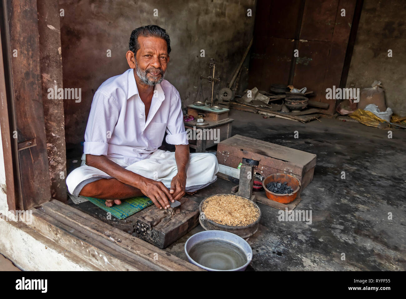 L'homme, l'attente pour les clients, assis en tailleur dans un magasin de la porte avec ses outils de travail en face de lui. Banque D'Images