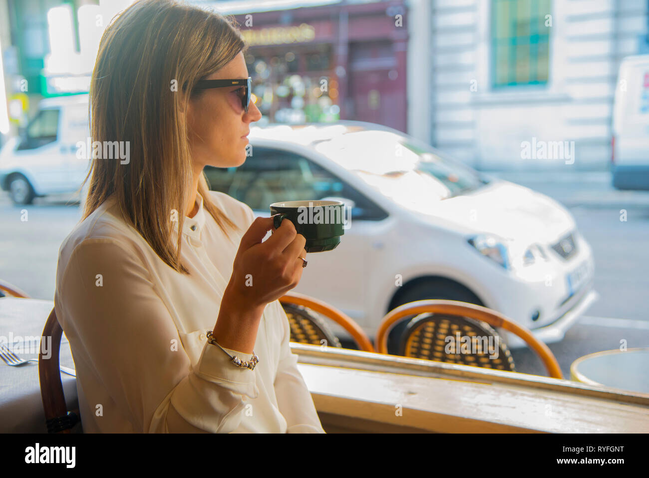 Jeune femme dans un café buvant du café et regardant la rue et sa voiture Banque D'Images