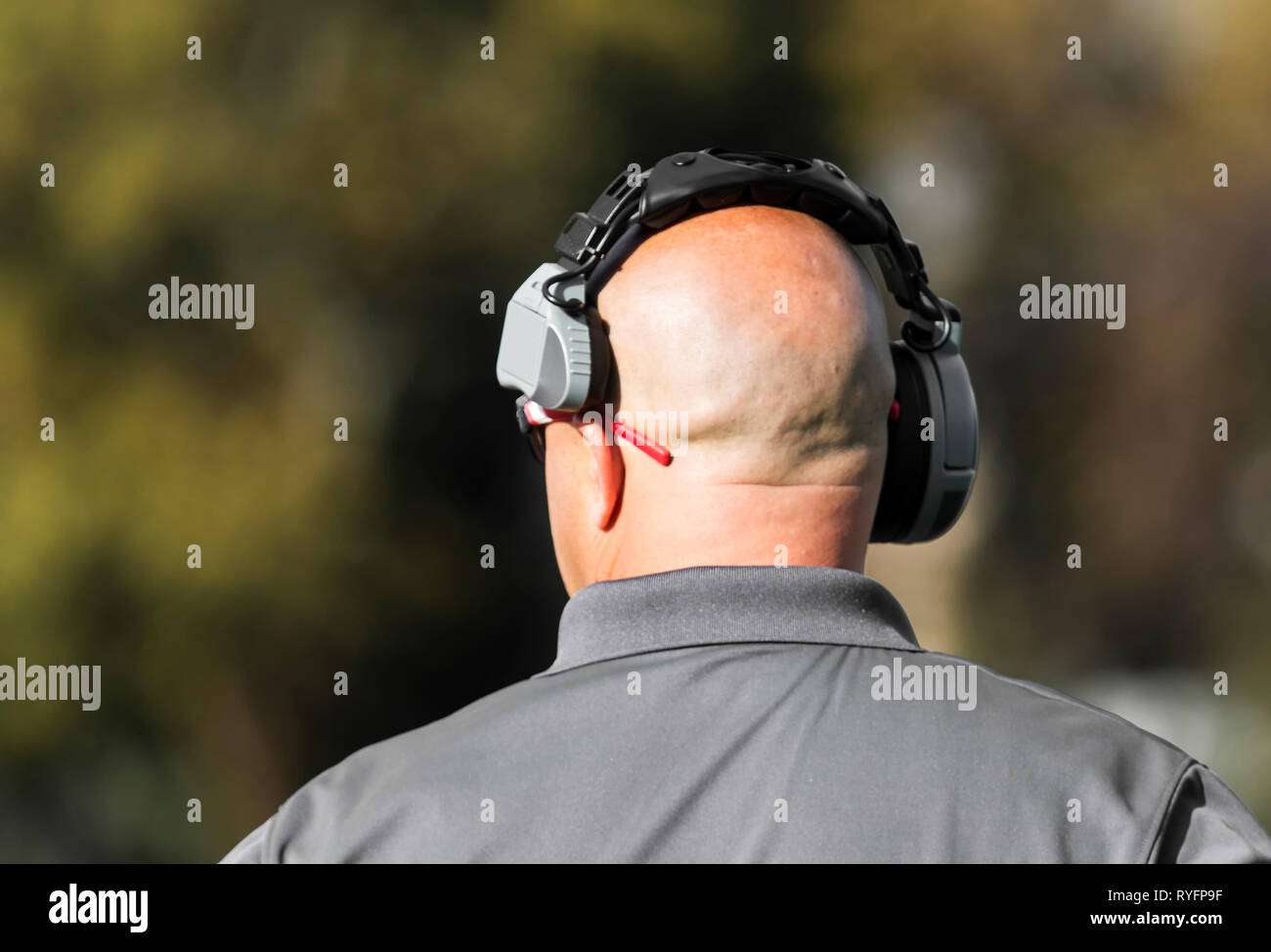 Un diplôme d'entraîneur de football a son casque sur tout en regardant vers le bas le champ à la jouer en cours d'exécution par son équipe. Banque D'Images