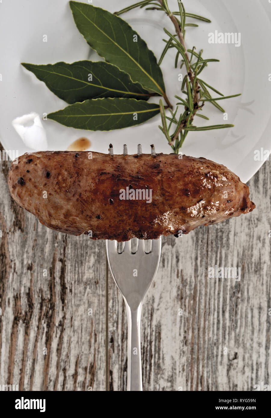 Salsiccia cotta su forchetta con piatto di erbe aromatiche primo piano Banque D'Images