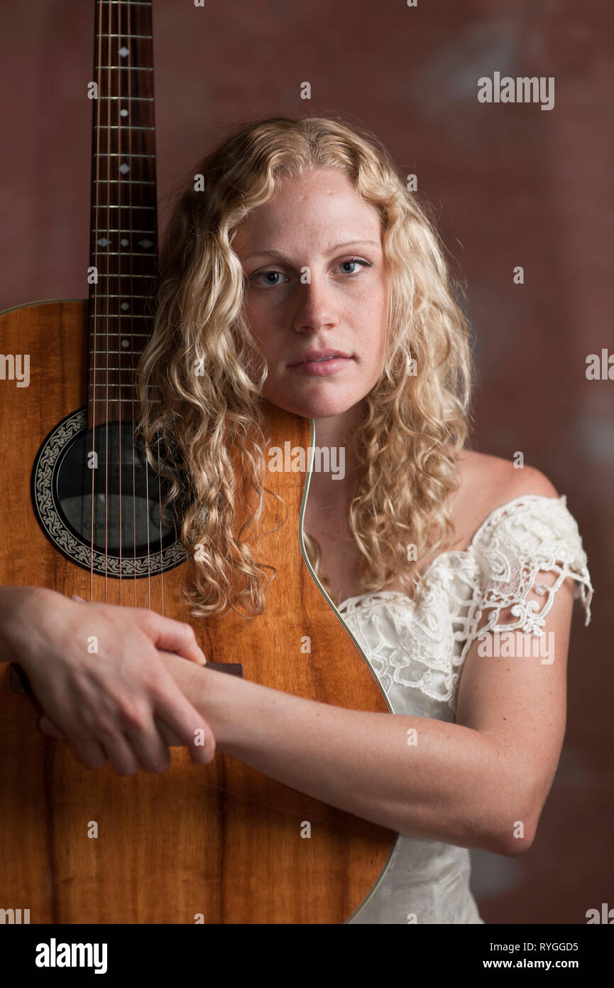 Portrait d'une jeune femme blonde avec de longs cheveux bouclés posant avec sa guitare Banque D'Images