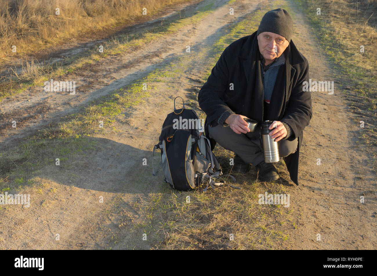 Randonneur fatigué est prêt à boire quelques tee tout en restant assis sur la route sale soirée d'automne à Banque D'Images