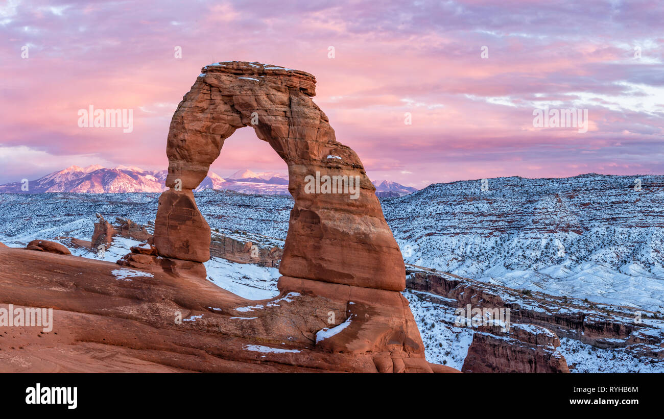 Un coucher de soleil colorés s'allume Montagnes La Sal derrière Delicate Arch iconique en février 2019 après une tempête de neige à Arches National Park, Moab, Utah. Banque D'Images