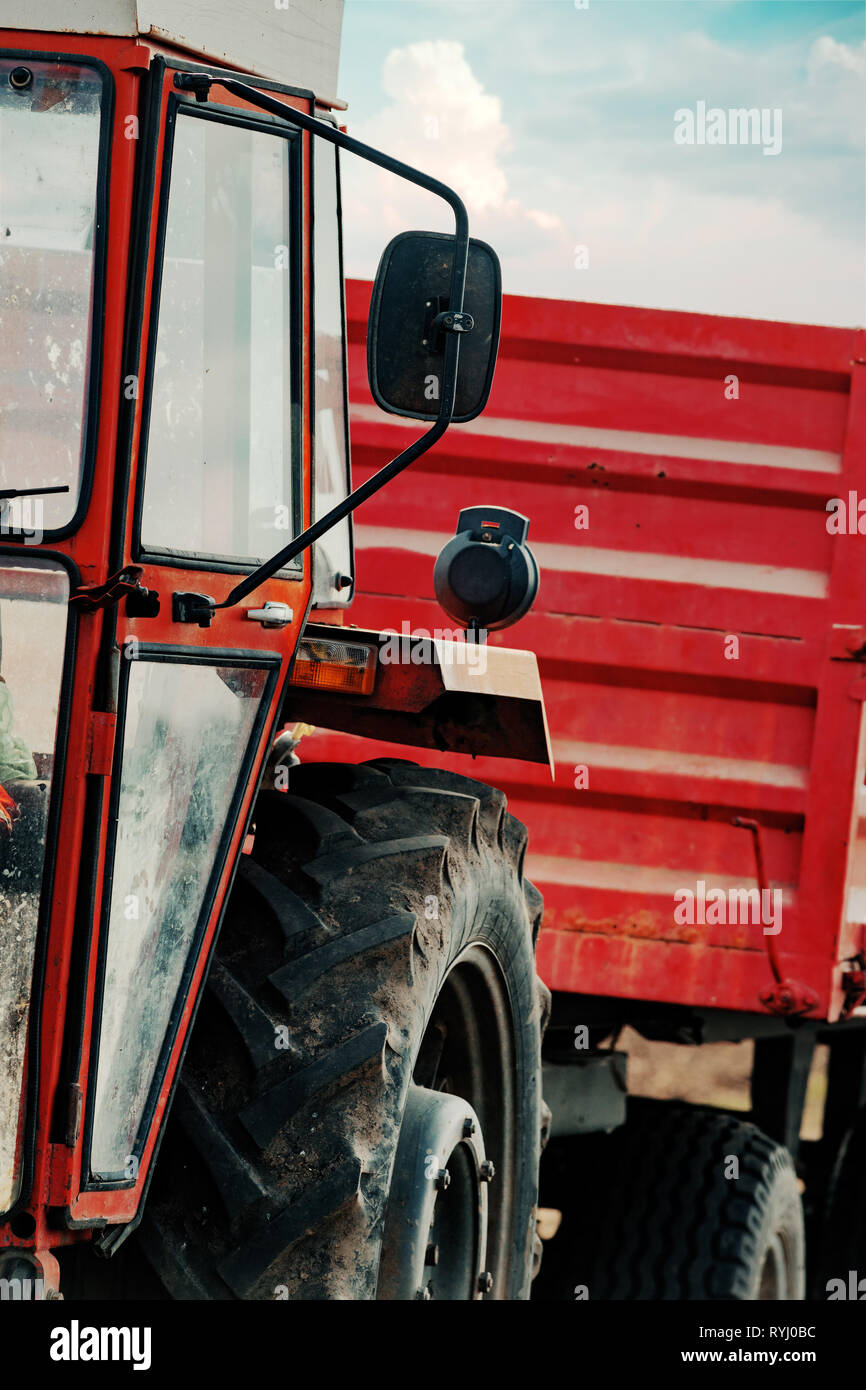 Vieux tracteur agricole rouge avec remorque sur la saleté route de campagne au printemps après-midi Banque D'Images