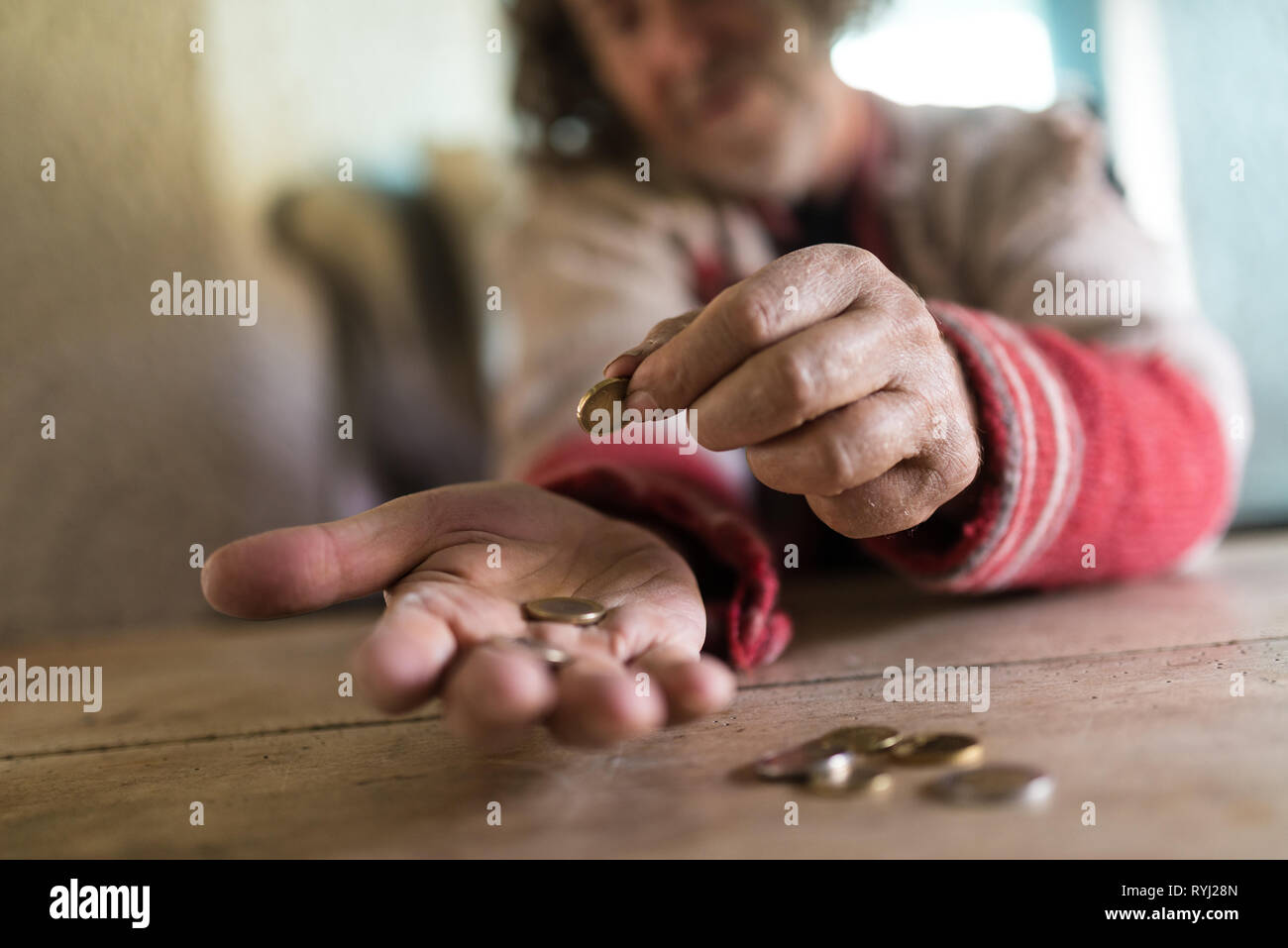 Portrait d'un vieil homme en chandail déchiré en comptant les pièces en euros sur un bureau en bois rustique dans une image conceptuelle. Banque D'Images