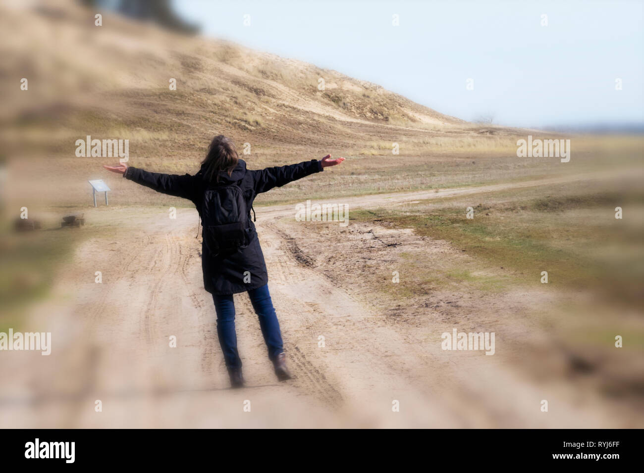 Caucasian woman in black coat bras levés sur la route vide vers le coucher du soleil l'horizontale Banque D'Images