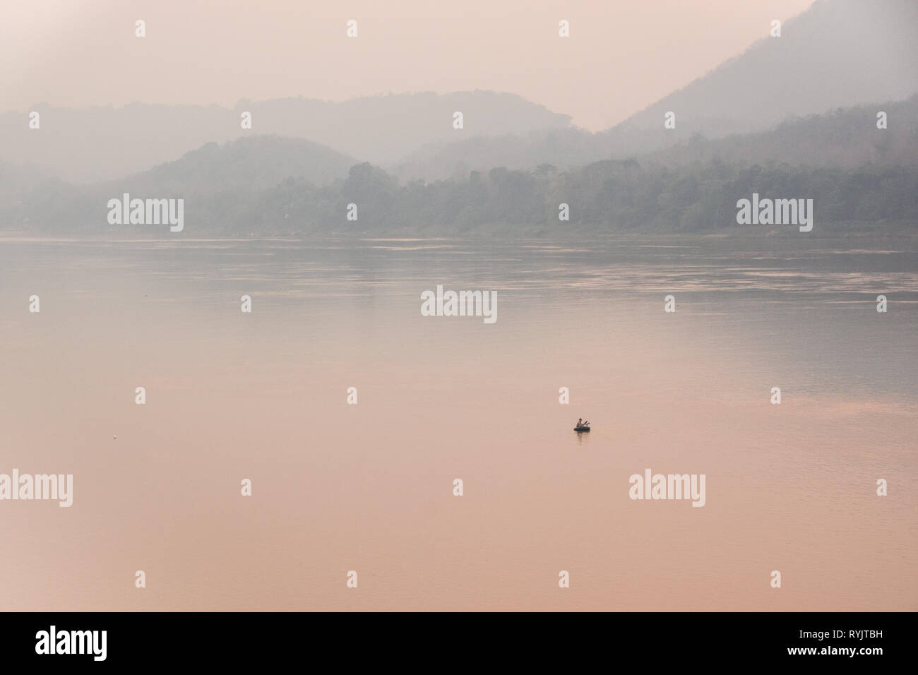 Perdu dans la brume sèche - Pêcheur sur un petit radeau sur la rivière du Mékong pendant la saison de gravure au Laos Banque D'Images