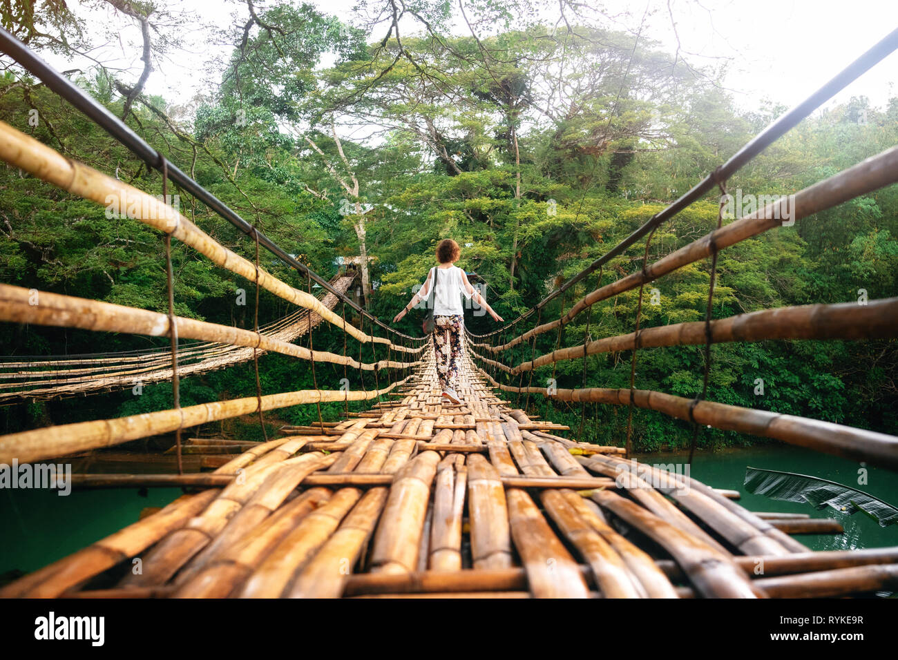 Vue arrière de jeune femme sur suspension bambou en bois pont à travers la rivière Loboc dans la jungle. Locations sur l'île tropicale. Bohol, Philippines Banque D'Images