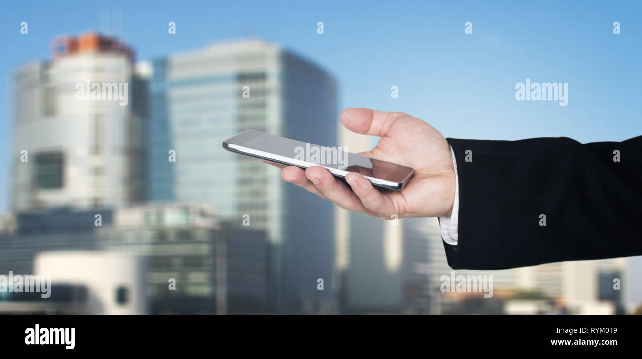 Businessmans Hand Holding Smartphone avec Cité des affaires et des bâtiments en arrière-plan Banque D'Images