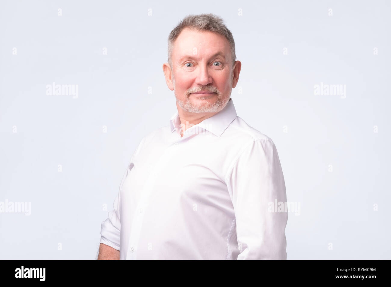 Smiling senior man in white shirt standing and smiling at camera sentiment bon Banque D'Images