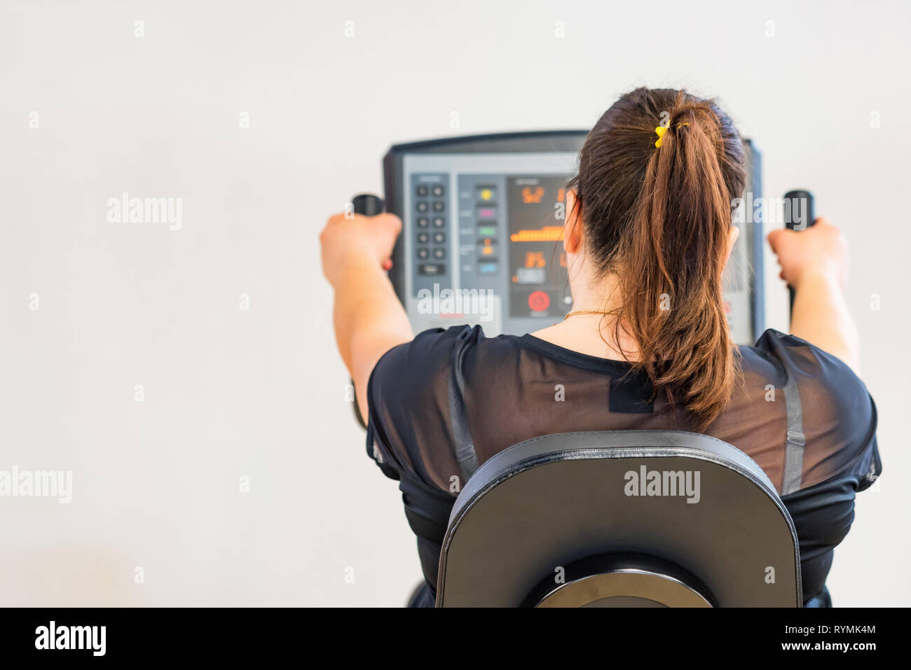 Vue arrière de jeune femme travaillant sur machine d'exercice dans la salle de sport Banque D'Images