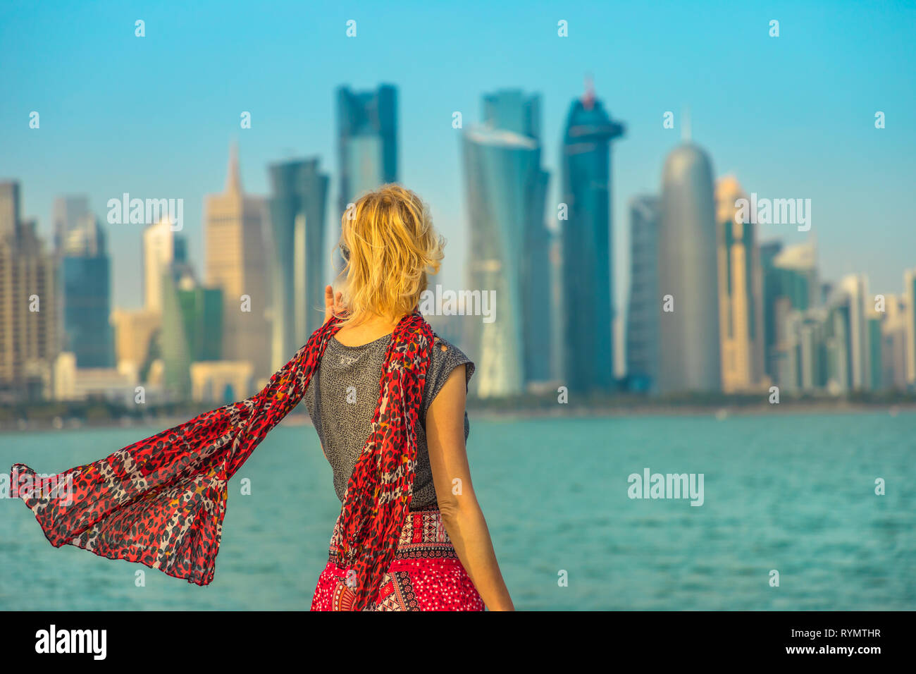 Retour de caucasian woman looking at gratte-ciel modernes de l'ouest le long de la baie de Doha Corniche, promenade sur la baie de Doha dans une journée ensoleillée. Visites touristiques femelle Banque D'Images