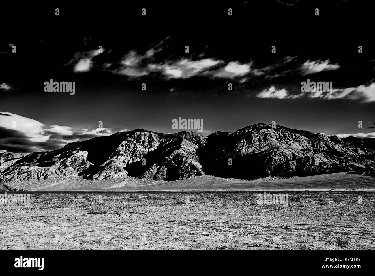 Ciel noir avec des nuages blancs, des montagnes avec des ombres profondes et désert aride valley . Banque D'Images