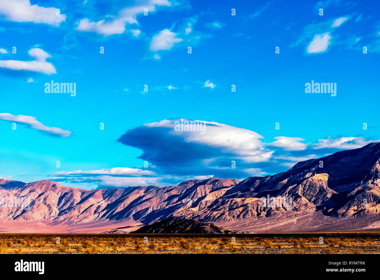 La vallée du désert avec des buissons morts et de montagnes stériles sous s ciel bleu avec des nuages. Banque D'Images