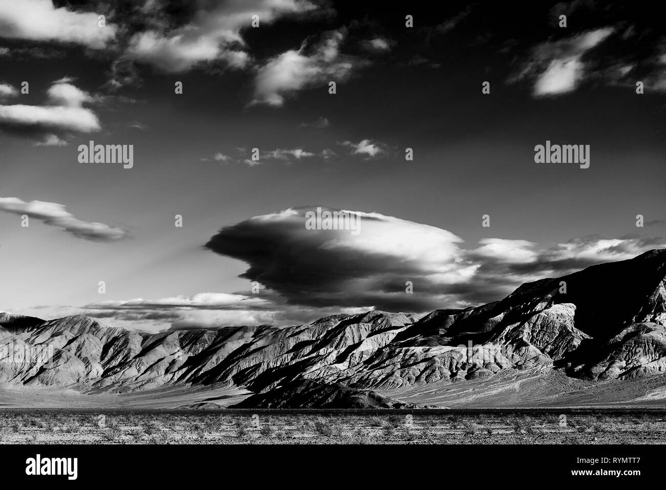 Noir et blanc, de la vallée du désert aride aux montagnes Rocheuses ; ciel avec des nuages blancs au-dessus. Banque D'Images