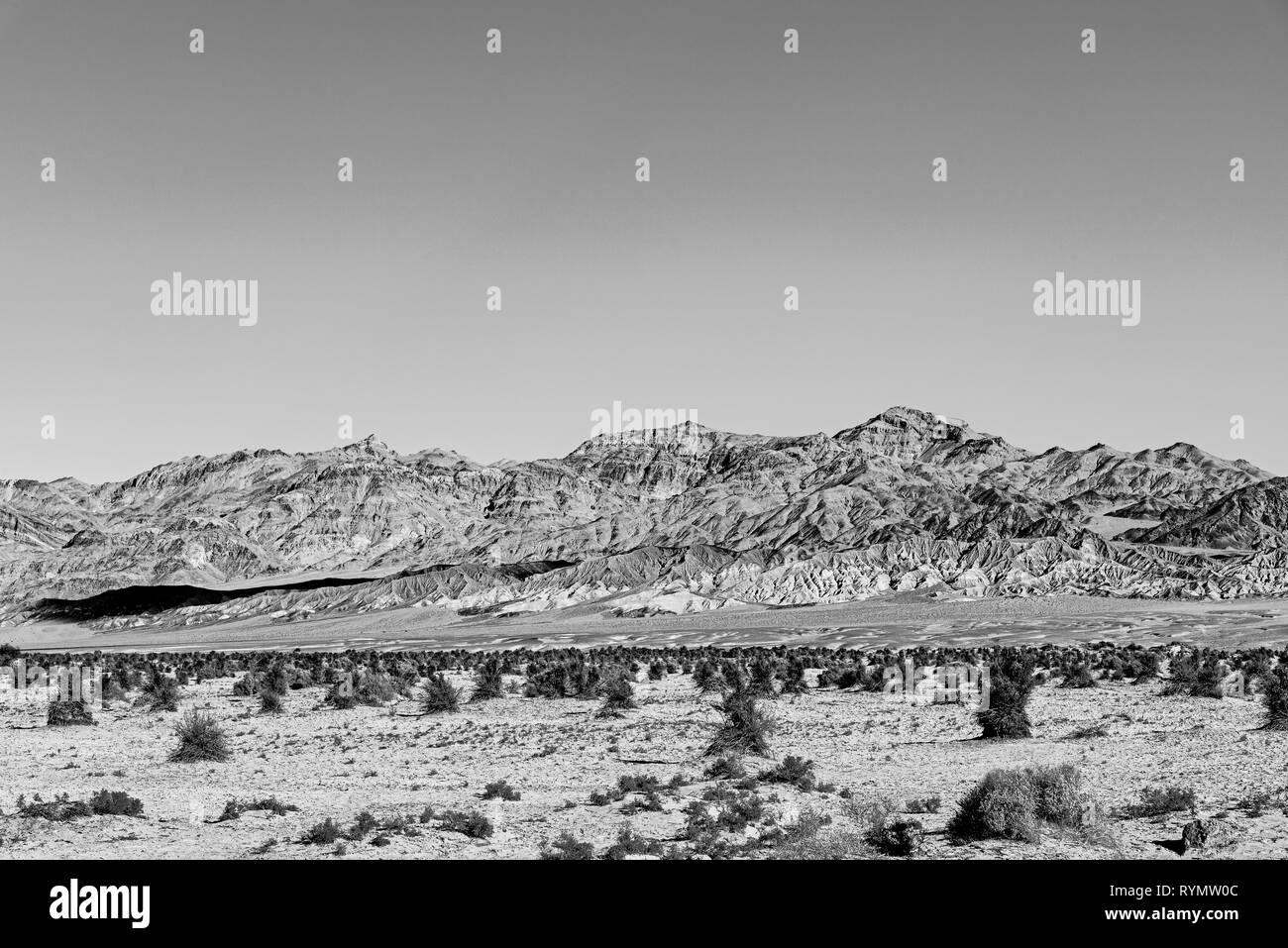 Le noir et blanc, de buissons de plus en plus désert de sable valley avec rocky montagnes stériles au-delà. Banque D'Images