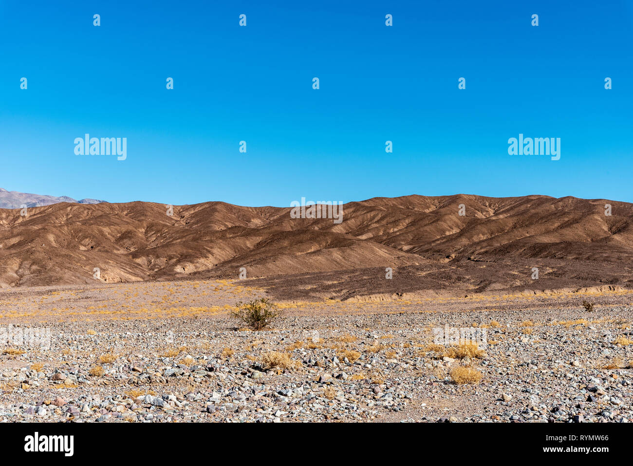 La végétation du désert rocheux Sparce sur vallée donnant façon de sécher brown montagnes stériles sous un ciel bleu. Banque D'Images