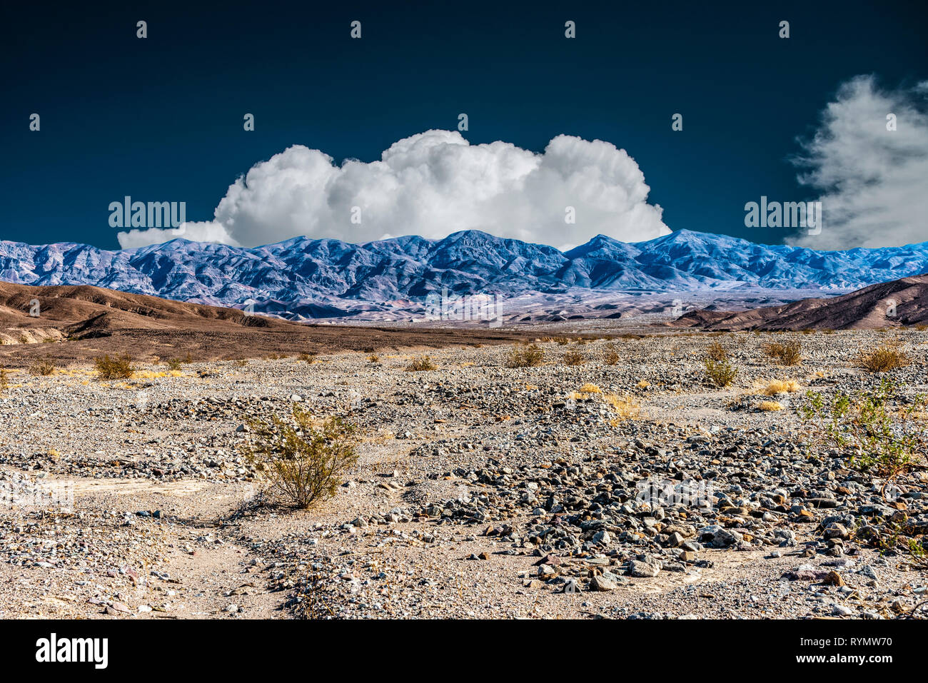 Infrarouge, vallée désertique rocheux avec brown hills place à des montagnes bleu sombre sous ciel bleu avec des nuages blancs moelleux. Banque D'Images