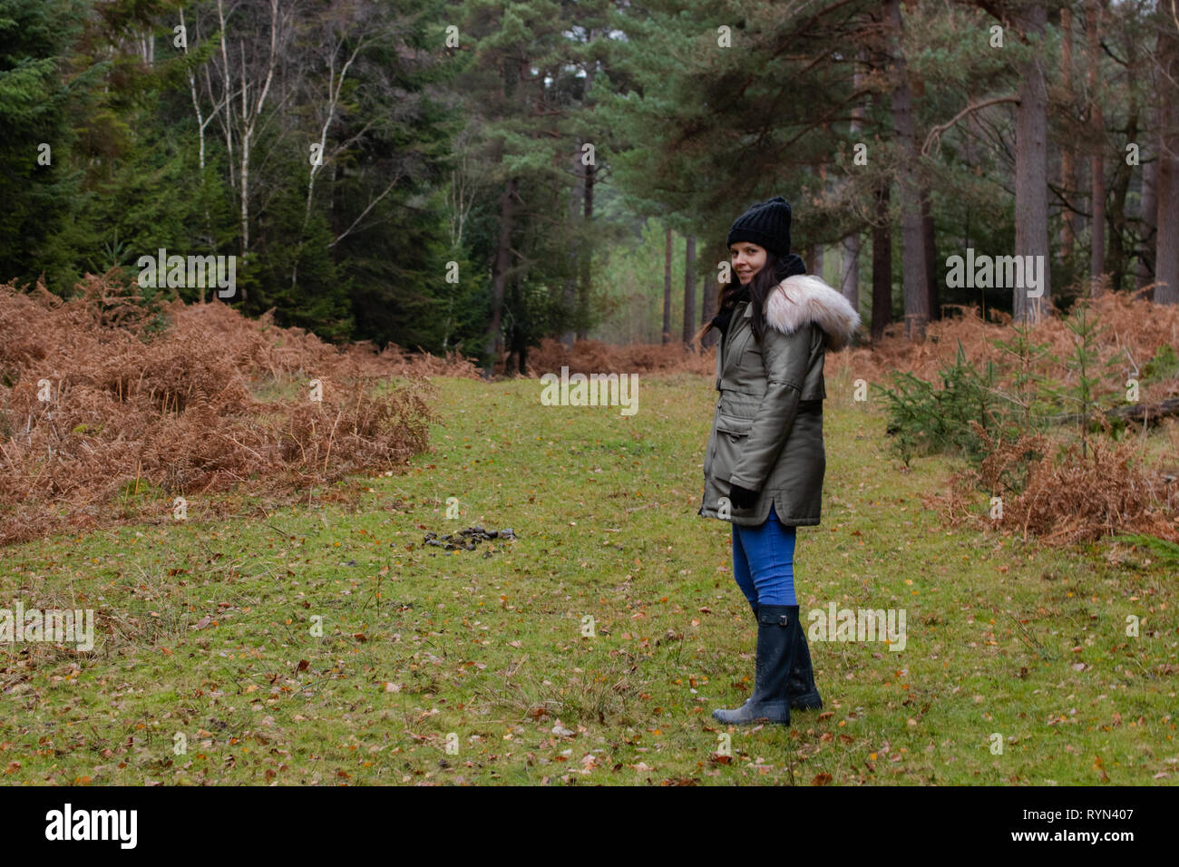 Femme en 30 ans se trouvait sur la voie de la forêt à la recherche de l'appareil photo, le port et un bobble hat wellies Banque D'Images