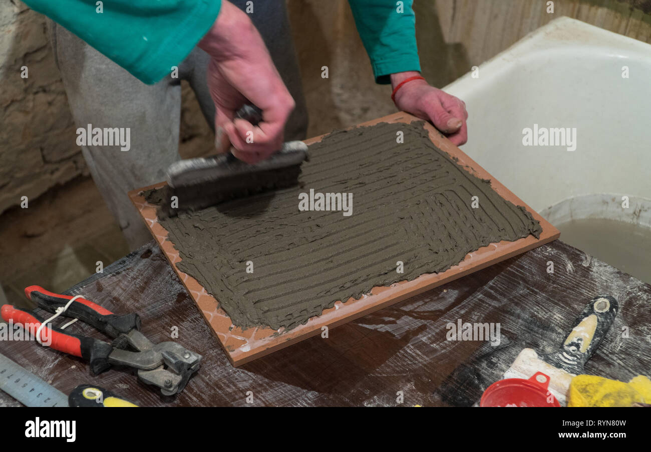 L'adhésif ciment travailleur s'applique sur les tuiles. Travaux de finition, de troubles de concentration. La technologie de pose de tuile. Banque D'Images