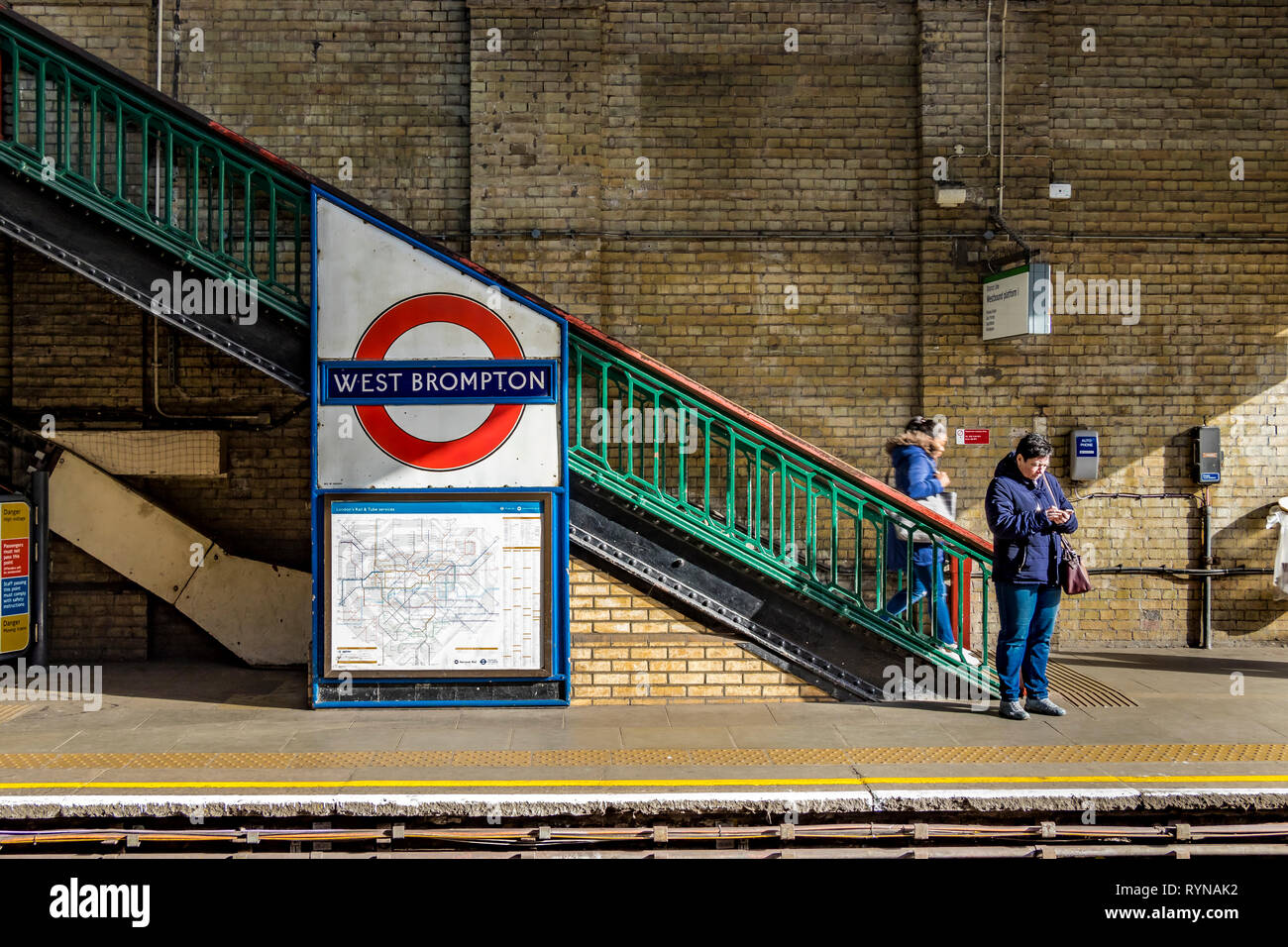 Une femme regarde son téléphone mobile en attendant un métro de la ligne de district de Wimbledon à la station de métro de West Brompton, Londres, Royaume-Uni Banque D'Images