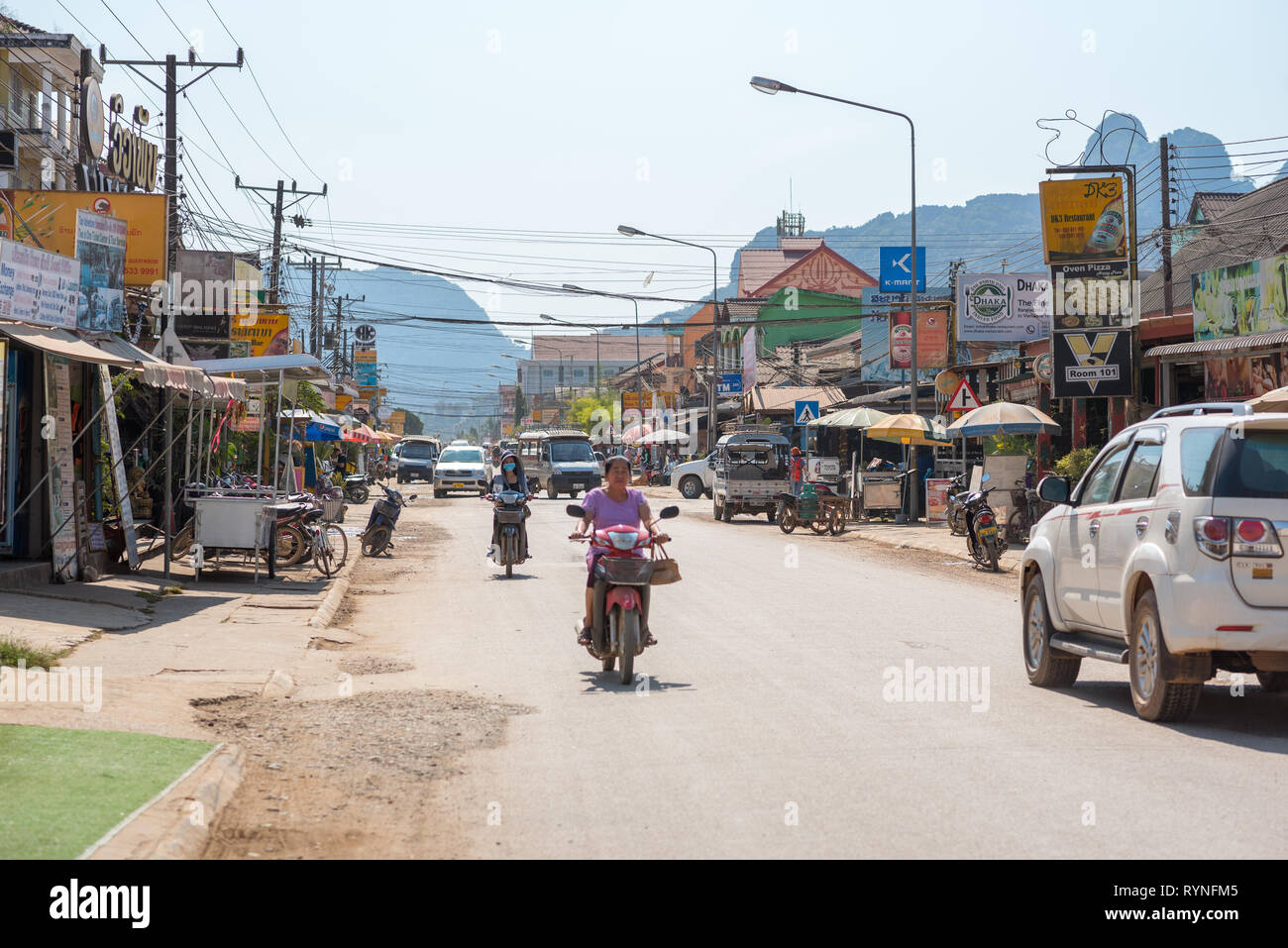 Vang Vieng, Laos - 28 décembre 2018 : rue principale de la ville avec la circulation, lampadaires et panneaux annoncer différents types d'entreprises touristiques. Banque D'Images