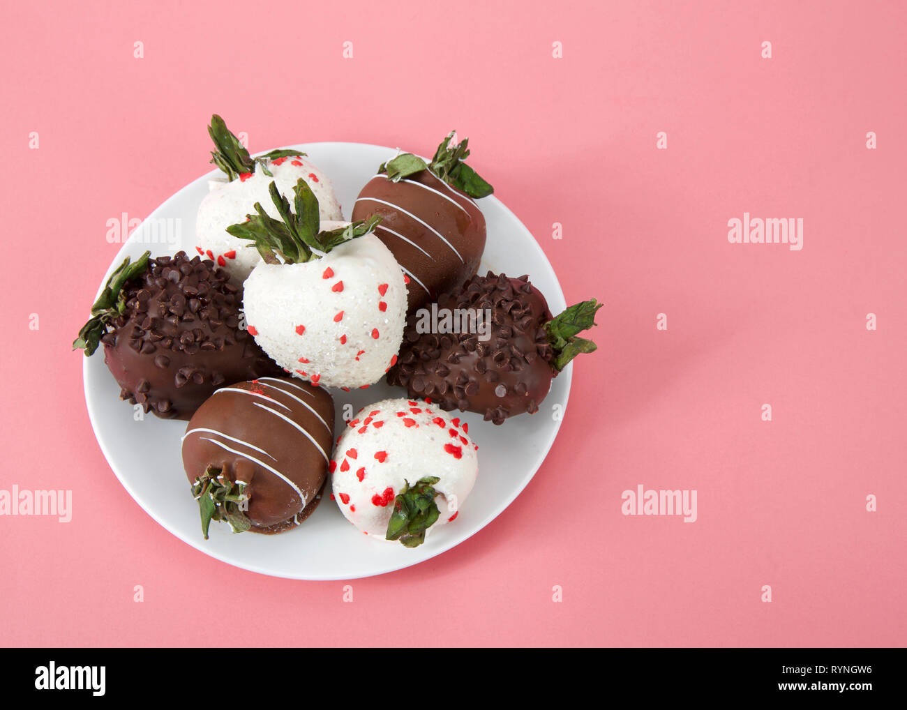 Variété de fraises enrobées de chocolat sur une assiette. Noir, blanc et de chocolat au lait sur fond rose. Vue d'en haut. Banque D'Images
