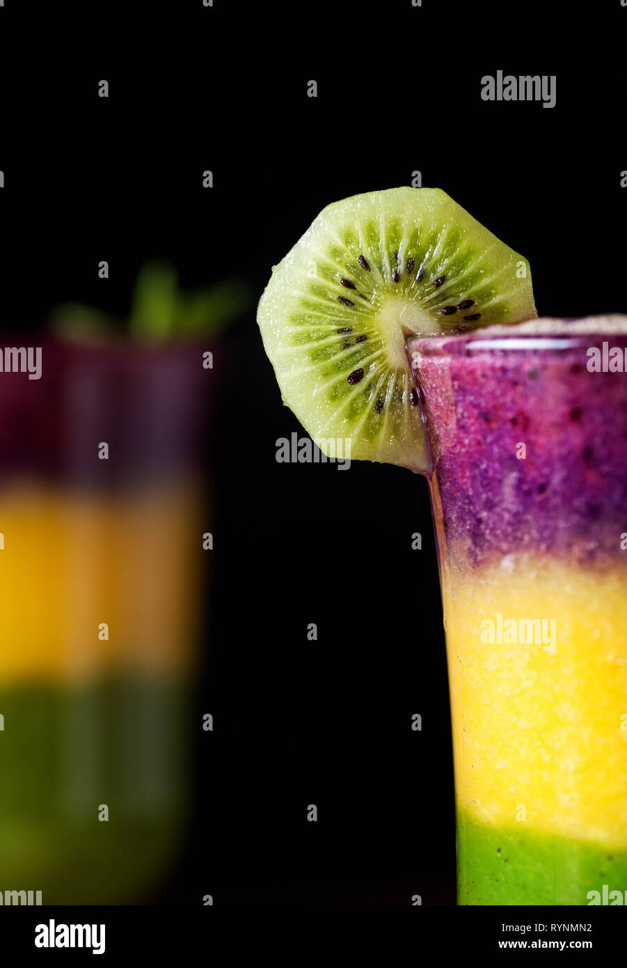 Verre de deux couches colorées avec smoothie de kiwi, oranges et blackberry sur fond noir close up Banque D'Images