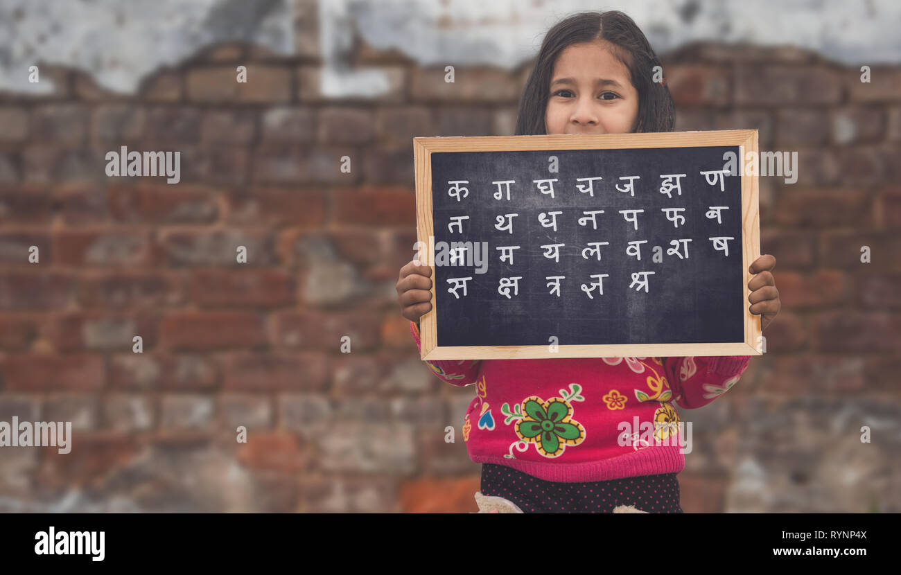 Adorable petit Indien 6-8 ans Filles asiatiques smiling holding, tableau de l'alphabet Hindi sur fond brique Banque D'Images