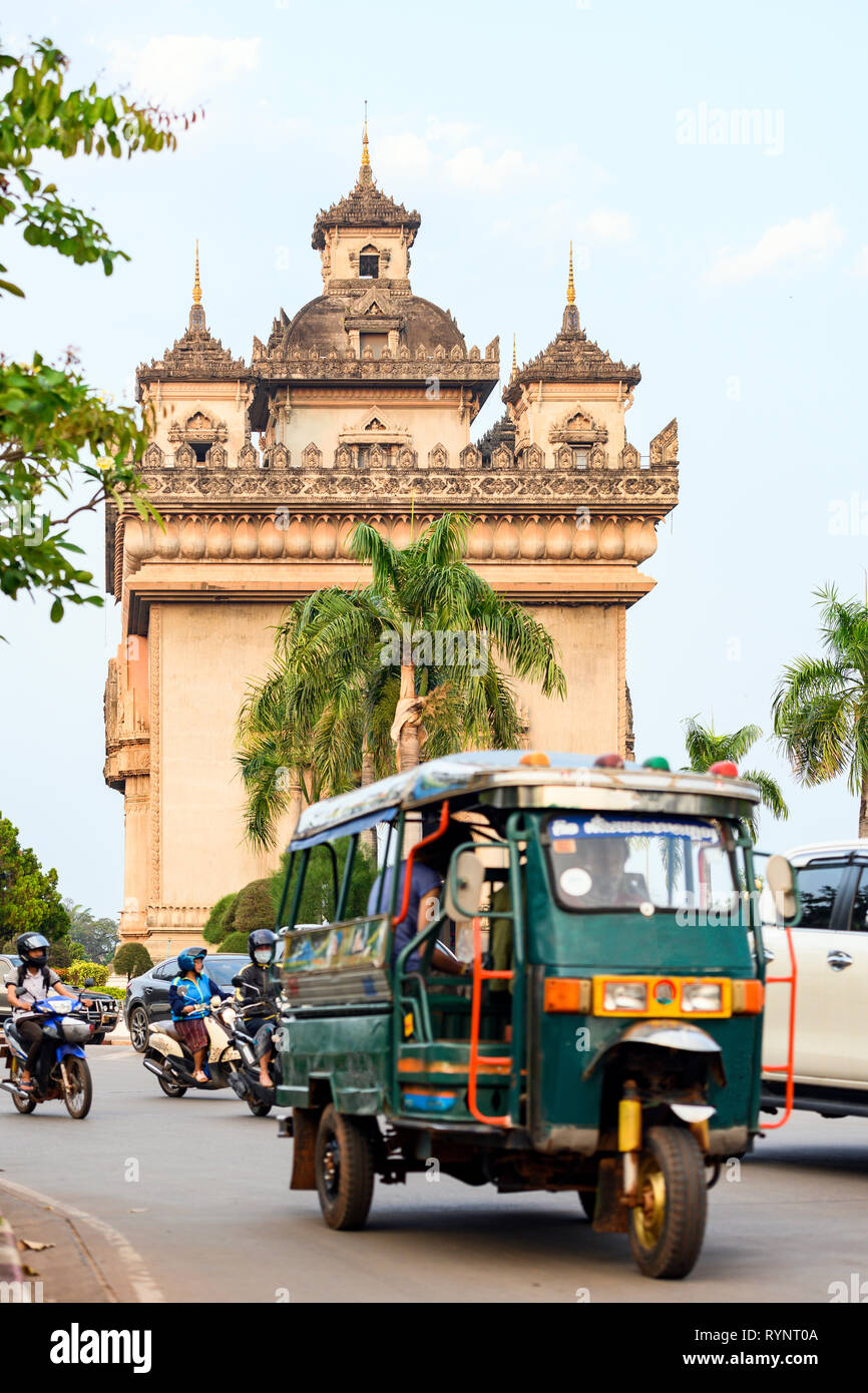 Vue imprenable sur la magnifique Patuxai avec voitures, motos et un Tuc Tuc traditionnels (auto rickshaw) passant au premier plan. Vientiane, Laos. Banque D'Images