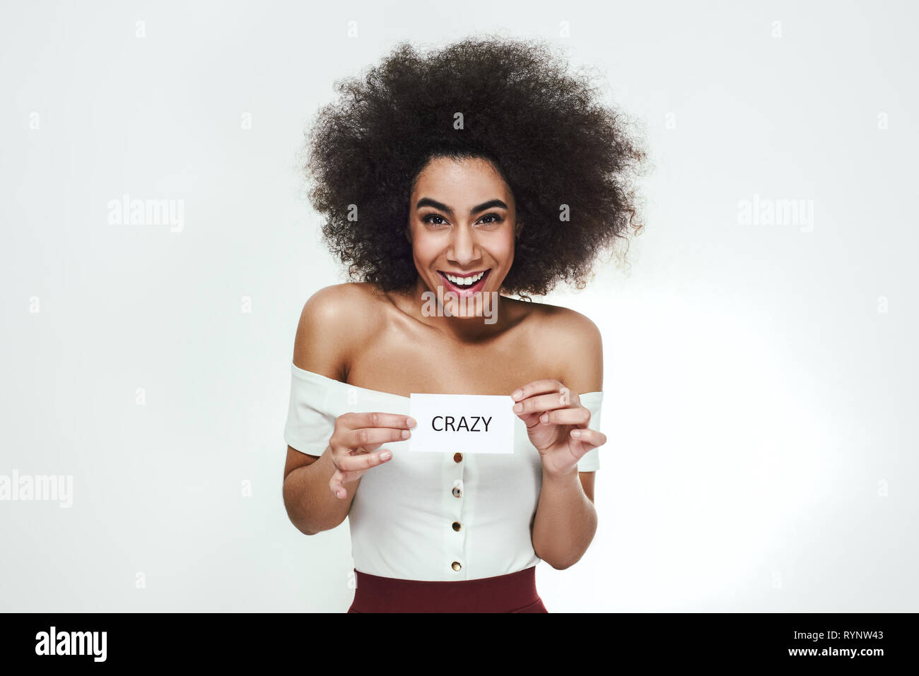 Complètement fous. Jeune femme africaine espiègle et souriant tenant un morceau de papier qui se dit 'crazy' debout contre un arrière-plan gris. Les émotions humaines. Portrait Studio Banque D'Images