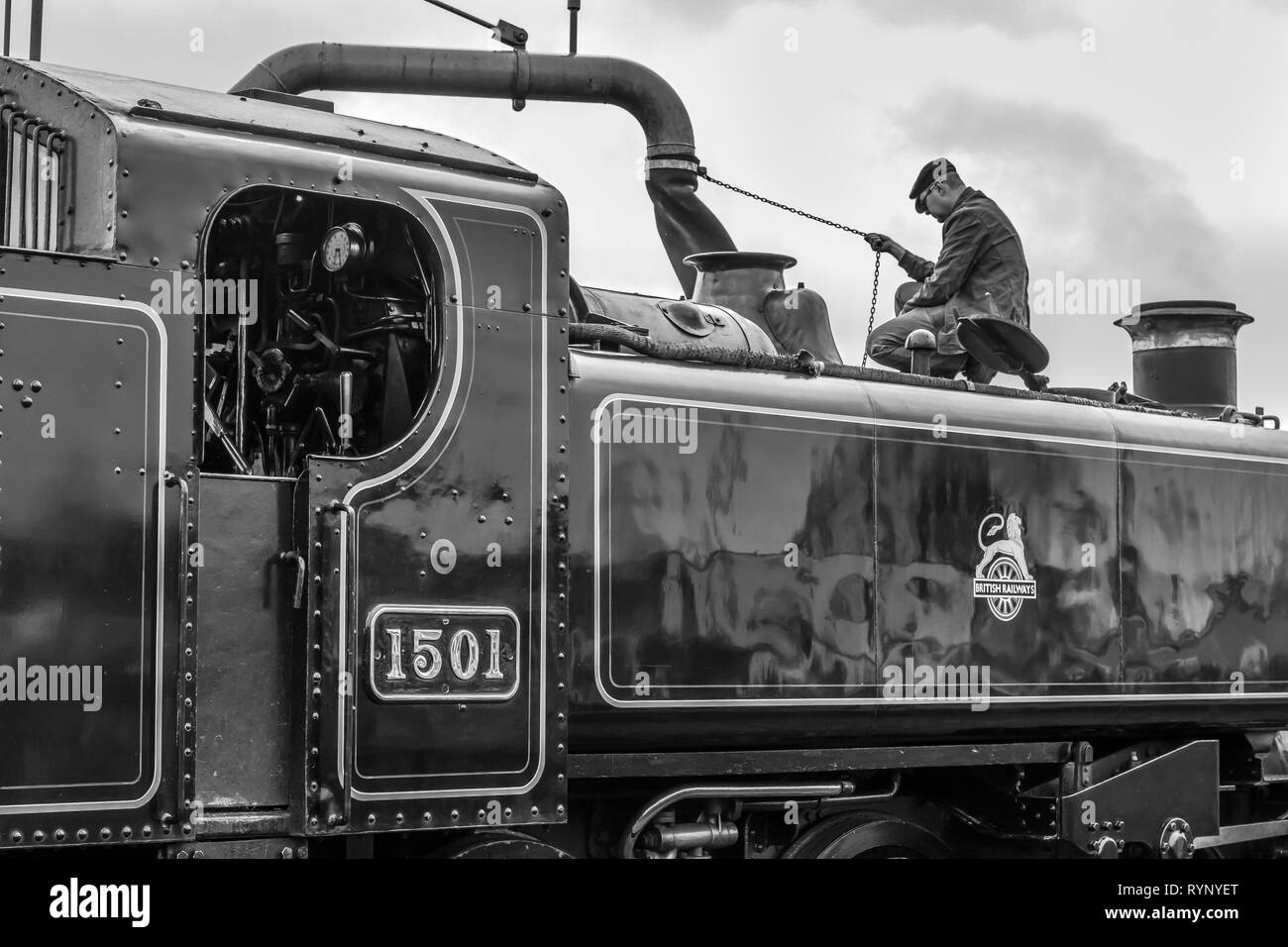 Noir et blanc, close-up side view of vintage UK locomotive à vapeur, arrêt prend l'eau. Conducteur de train, vue latérale, sur machine à vapeur du remplissage du réservoir. Banque D'Images