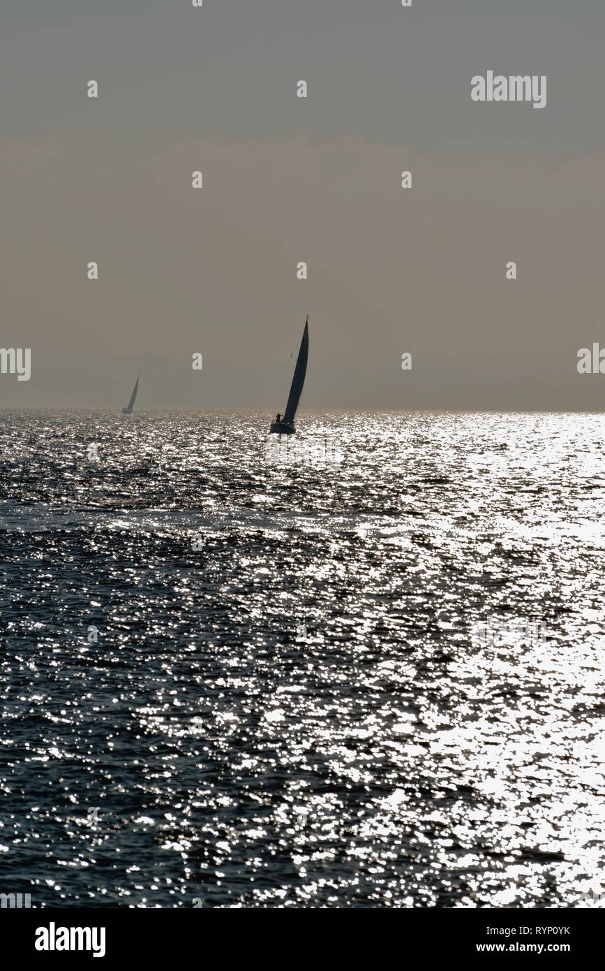 Silhouette d'un voilier naviguant sur le Solent à Portsmouth, Hampshire contre la réflexion de la lumière du soleil sur la mer, en Angleterre, Royaume-Uni Banque D'Images