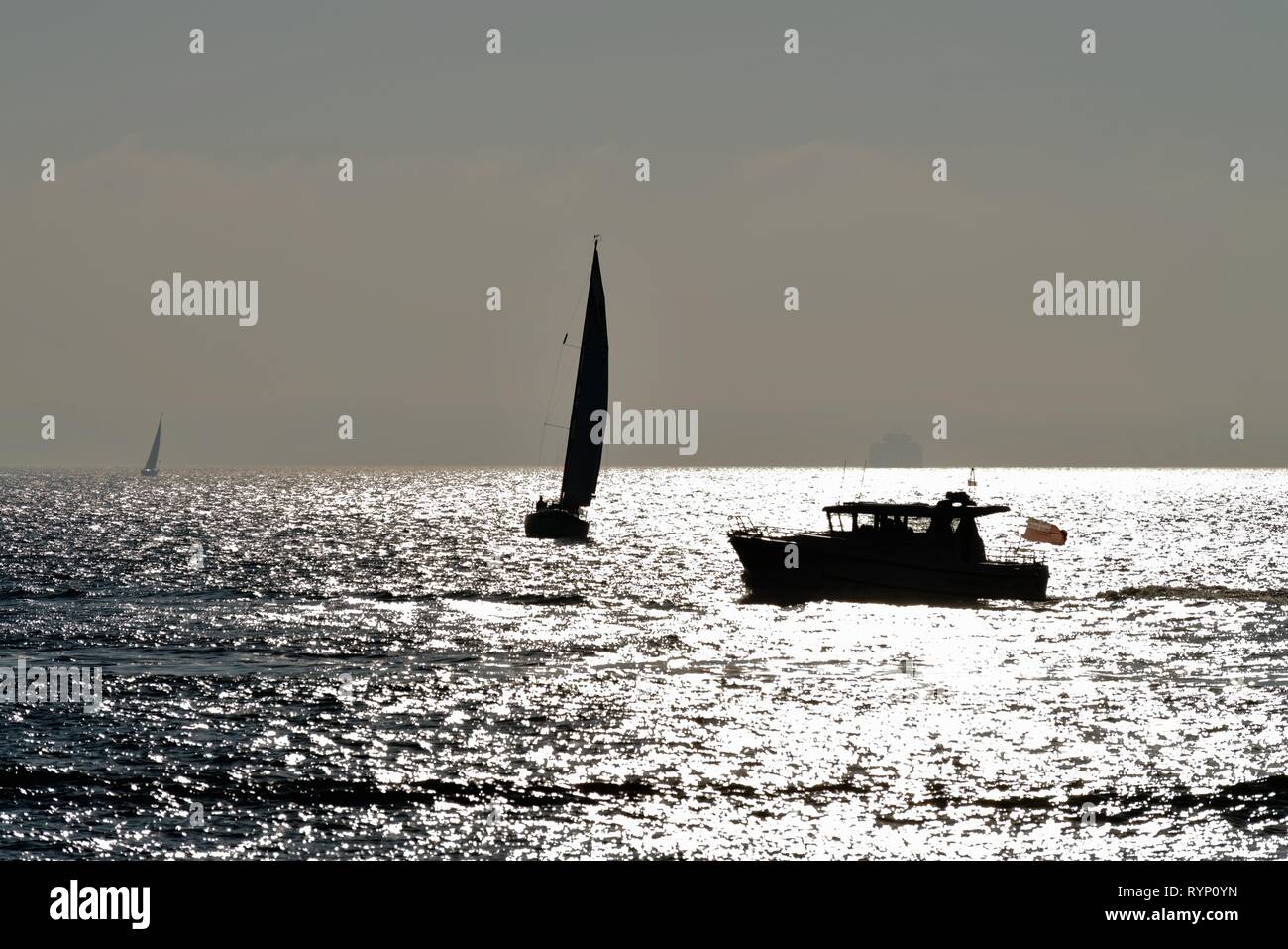 Silhouette d'un yacht à moteur et la voile sur le Solent à Portsmouth, Hampshire contre la réflexion de la lumière du soleil sur la mer, en Angleterre, Royaume-Uni Banque D'Images