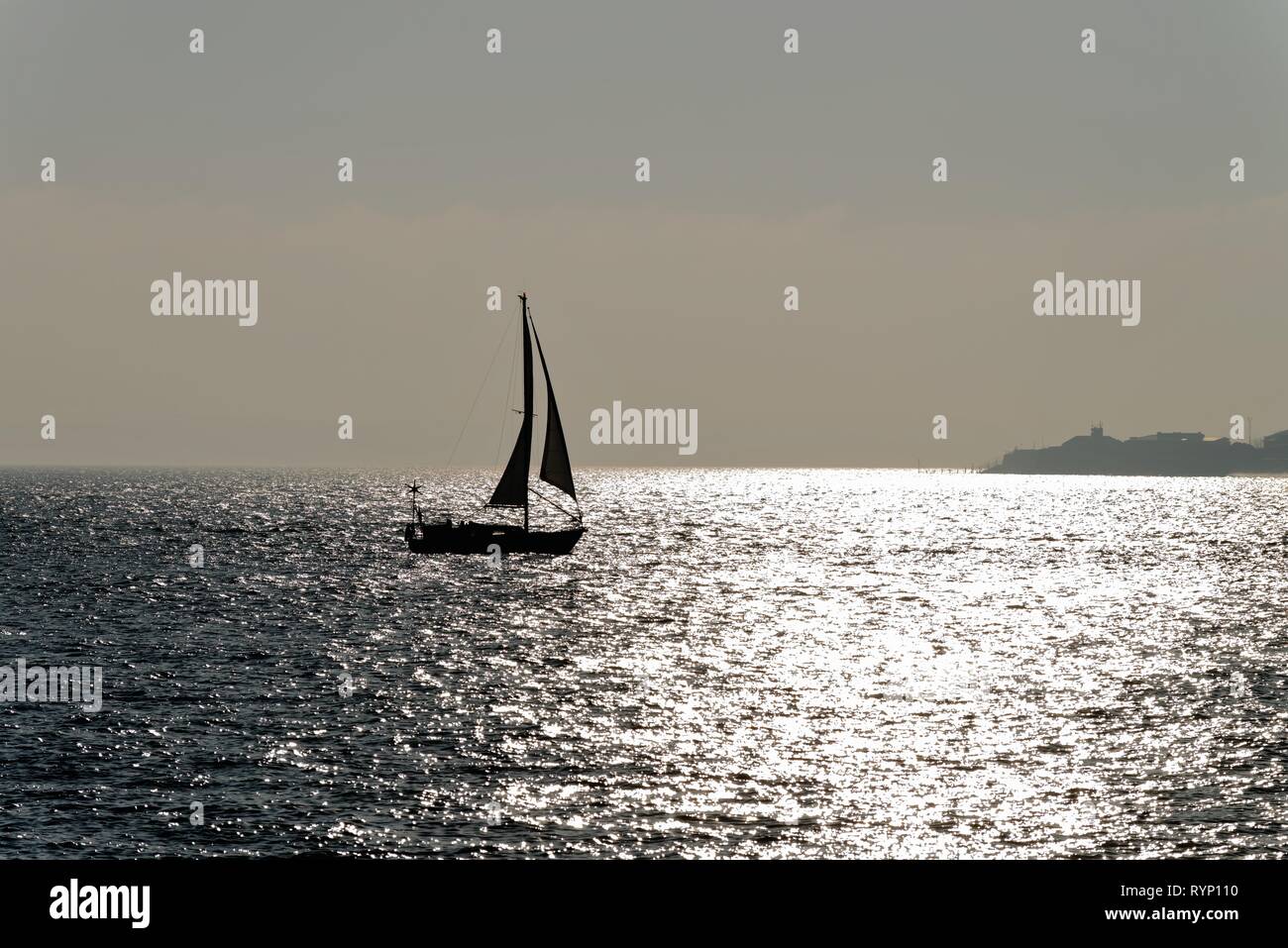 Silhouette d'un voilier naviguant sur le Solent à Portsmouth, Hampshire contre la réflexion de la lumière du soleil sur la mer, en Angleterre, Royaume-Uni Banque D'Images