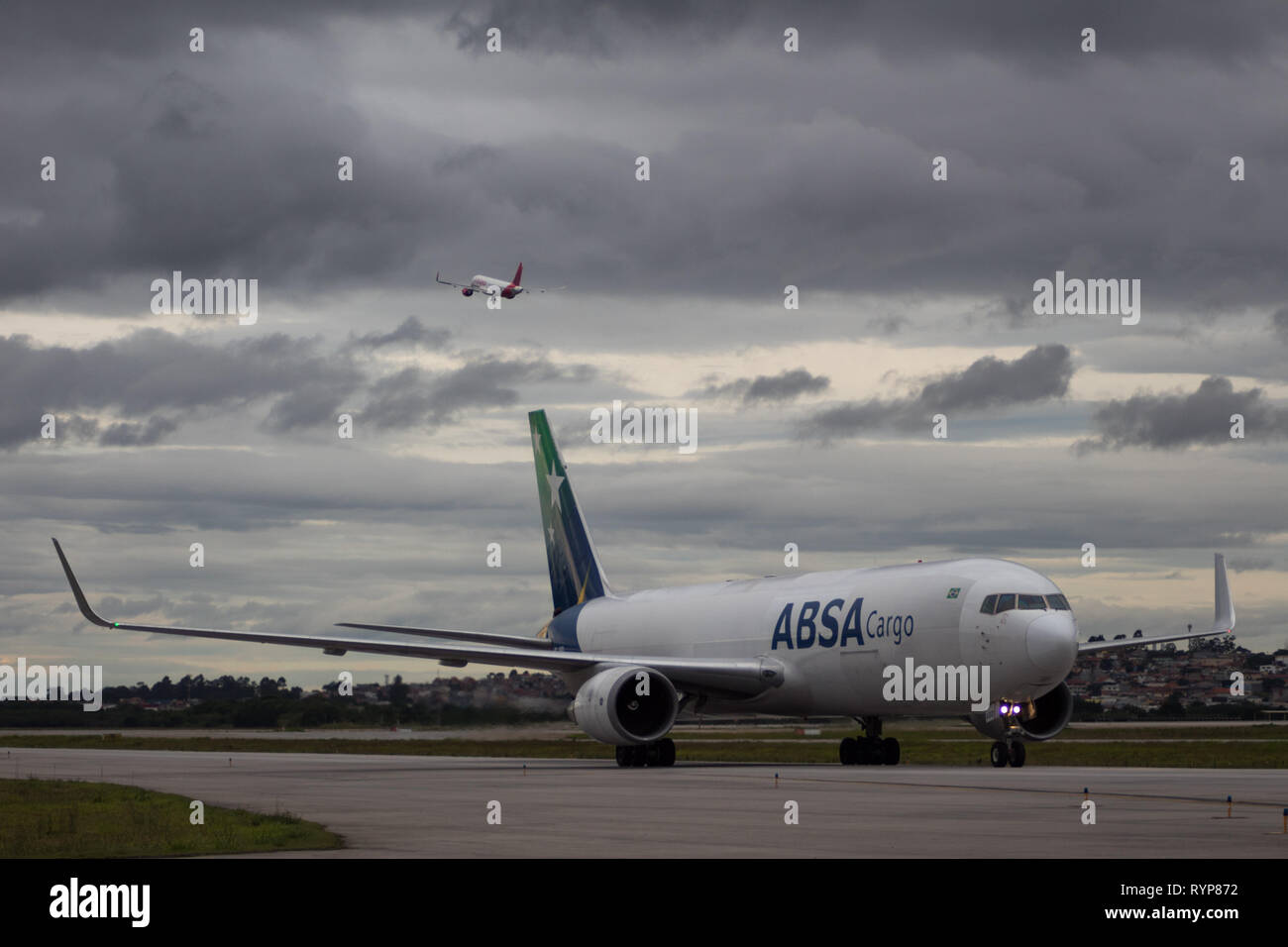 Boeing 767-300F de l'ABSA Cargo Airlines roulait dans l'aéroport de Guarulhos, tandis qu'un autre avion décolle. Banque D'Images