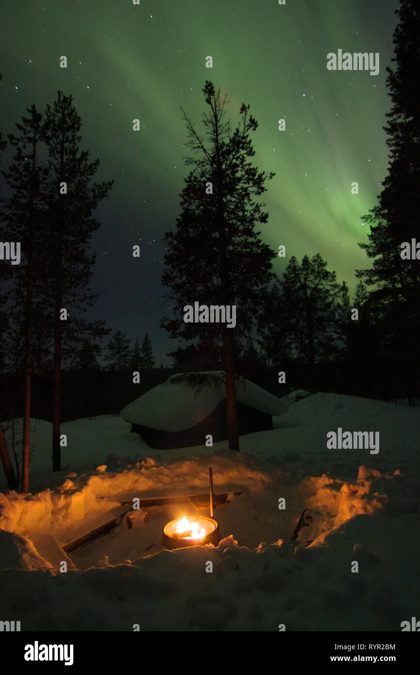 Cheminée avec un cottage en bois et des arbres couverts de neige derrière et aurora borealis (northern light) ci-dessus sur une nuit d'hiver en Laponie finlandaise. Sarre Banque D'Images